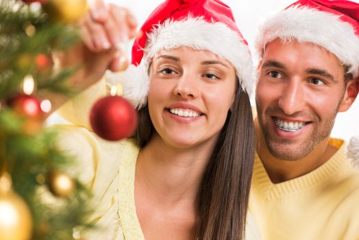 Happy young couple enjoy decorating Christmas tree at home. Selective Focus, focus on couple.