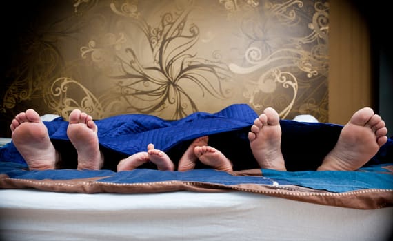 Four pairs of legs of the happy family in bed - father, mother and children