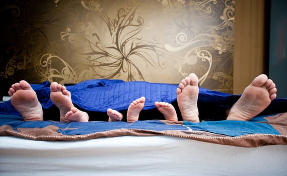 Four pairs of legs of the happy family in bed - father, mother and children