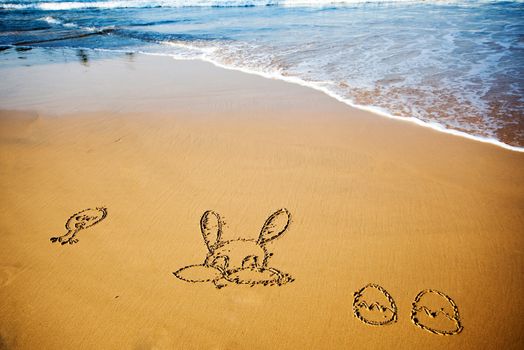 Easter bunny and eggs drawn in sand on tropical beach