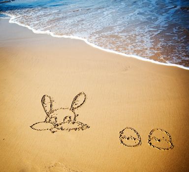 Easter bunny and eggs drawn in sand on tropical beach