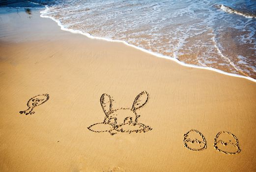 Easter bunny and eggs drawn in sand on tropical beach