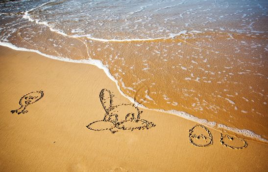 Easter bunny and eggs drawn in sand on tropical beach