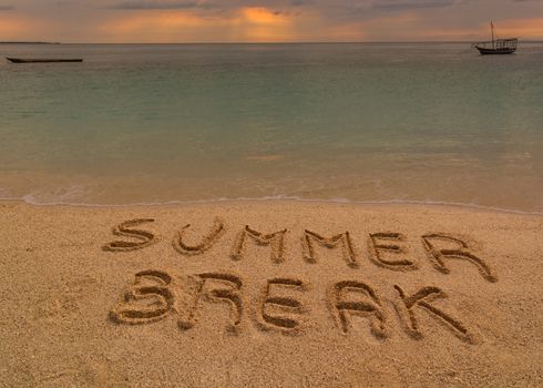 In the picture a beach at sunset with the words on the sand "Summer break".