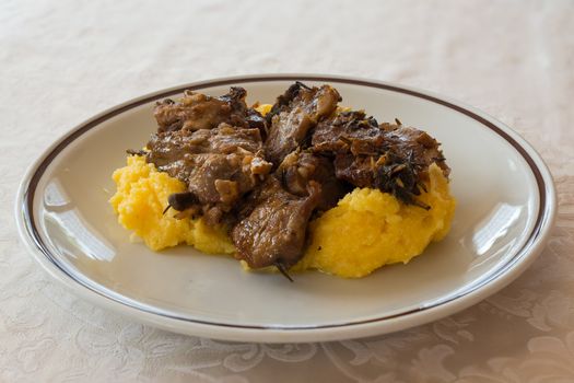 in the picture typical italian food ,roasted goat and Polenta on white dish at restaurant.