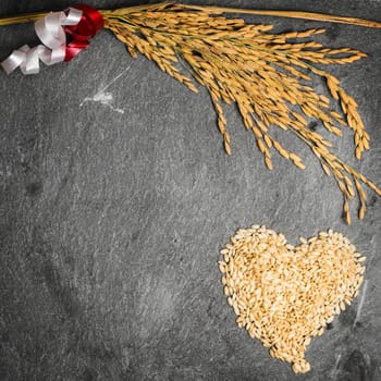 In the picture an ear of wheat and a heart formed by grains of rice on background of  stone.