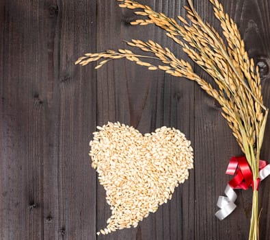 In the picture an ear of wheat and a heart formed by grains of rice on background of wood