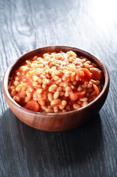 Wooden bowl full of stewed beans on wooden background