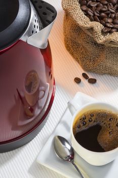 A cup of fresh coffee with a reflection on the side of a kettle