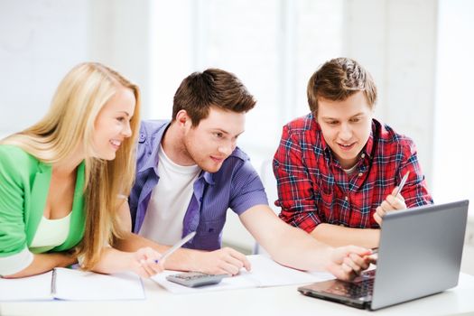 education concept - smiling students looking at laptop at school