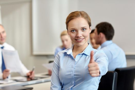 business, people, gesture and teamwork concept - smiling businesswoman showing thumbs up with group of businesspeople meeting in office