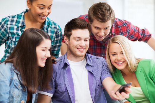 education concept - group of students looking into smartphone at school