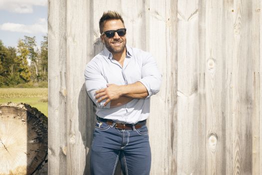 A handsome man outdoor in front of a wooden background wall