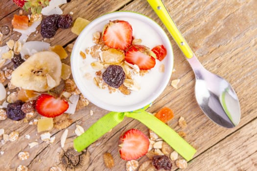 yogurt with cereals muesli, fresh strawberries, banana and raisins in bowl on wooden background