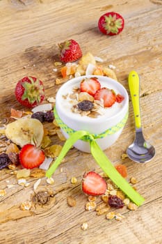 yogurt with cereals muesli, fresh strawberries, banana and raisins in bowl on wooden background