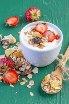 yogurt with cereals muesli, fresh strawberries, banana and raisins in bowl on wooden background