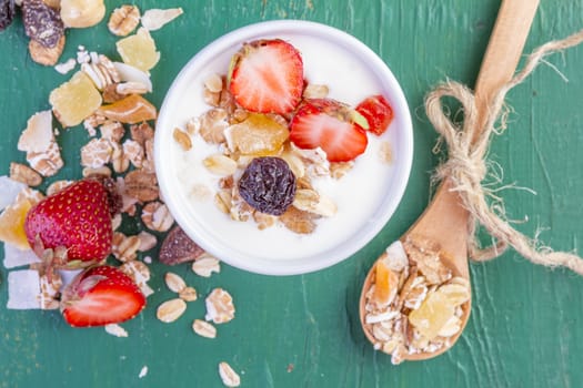 yogurt with cereals muesli, fresh strawberries, banana and raisins in bowl on wooden background