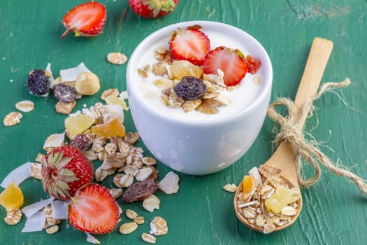 yogurt with cereals muesli, fresh strawberries, banana and raisins in bowl on wooden background