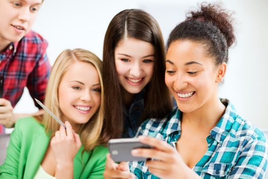 education and internet - smiling students looking at smartphone