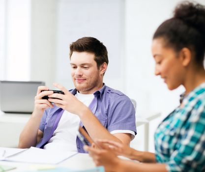 education concept - students looking at phones and tablet pc at school