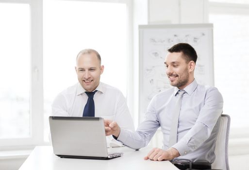 business, technology and office concept - two smiling businessmen with laptop in office