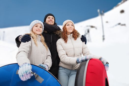 winter, leisure, sport, friendship and people concept - group of smiling friends with snow tubes over mountain background