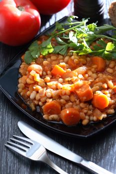 Black plate full of stewed beans on wooden background