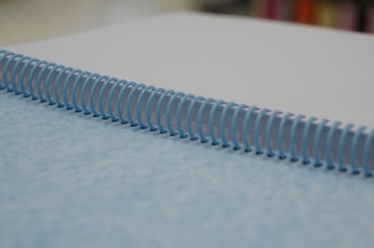 Blank notebook with blue spiral spine is opened on table at office.                             