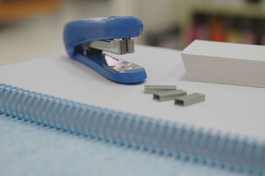 Blue stapler and three staples placed on book at office.                         