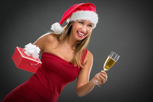 Cheerful beautiful young woman in red dress with Christmas gift toasting with champagne.