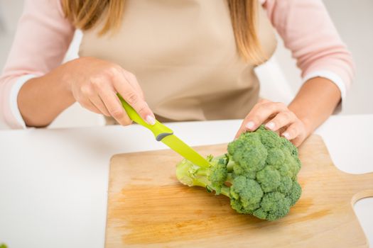 Close-up of a female hands cutting broccoli on the kitchen board.