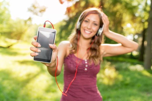 Happy beautiful girl listening music from smart phone in the park. Focus on the phone.