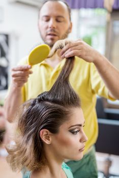 Hairdresser combing long brown hair with brush and making hairstyle. 