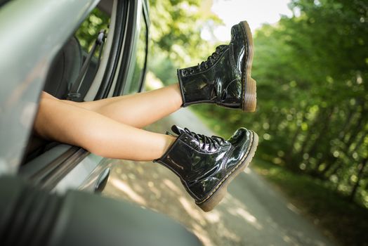 Girl resting on the side of a road and stretching her legs out the window of car.