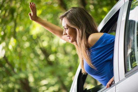 Young beautiful woman waving through the open window of a car. 