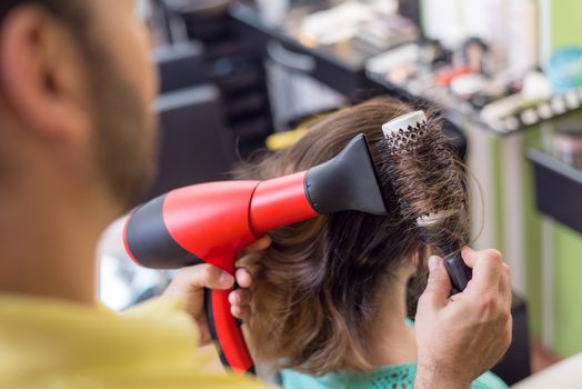 Hairdresser drying long brown hair with round brush. 