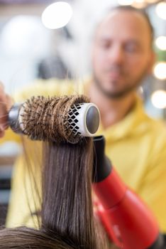 Close up of a drying long brown hair with round brush. 