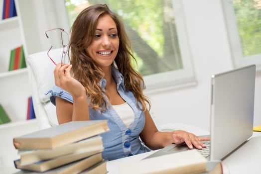 Beautiful teenage girl with many books and laptop learning in the library.