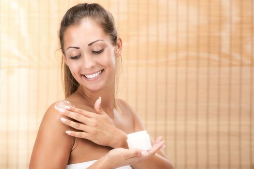 Cute girl preparing to start her day. She is applying body lotion and smiling.