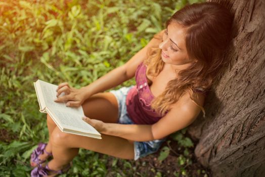 Portrait of a beautiful smiling Girl reading book in the park.