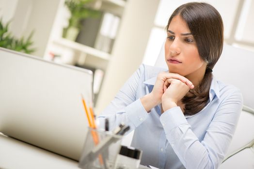 Portrait of a thinking businesswoman sitting in the office and looking at laptop.