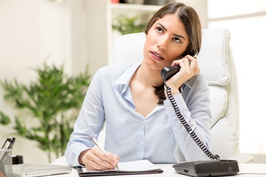 A young thinking businesswoman phoning in office