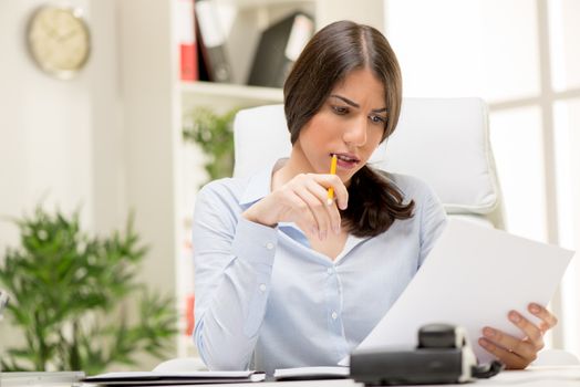 Portrait of a beautiful young businesswoman sitting in the office, biting pen and thinking.