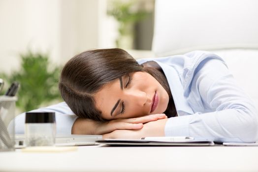 Young businesswoman sleeping on her desk next to documents late in the office.