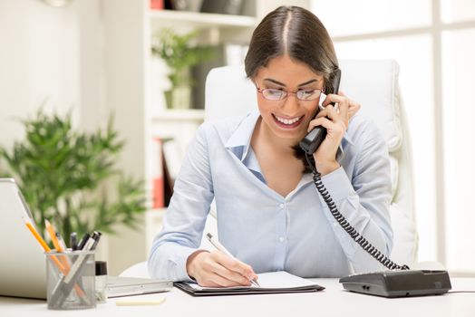 A young beautiful businesswoman sitting in the office and phoning.