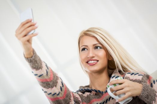 Portrait of pretty young woman taking a self-portrait with her smartphone at home.