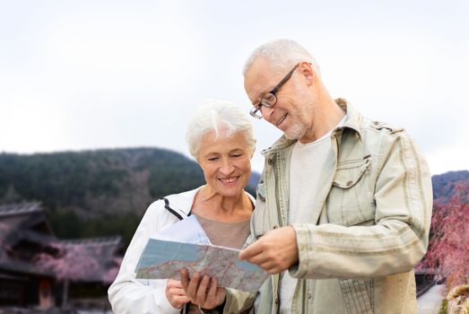 family, age, tourism, travel and people concept - senior couple with map and over asian village and mountains landscape background