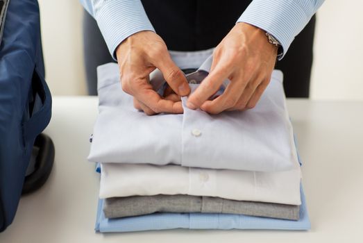 business, trip, luggage and people concept - close up of businessman packing clothes into travel bag