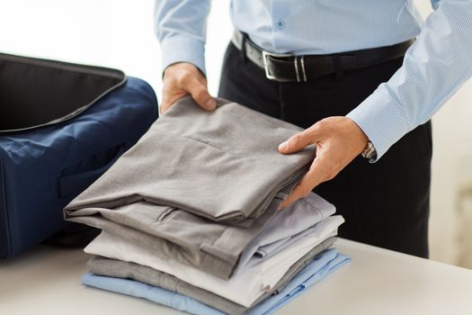 business, trip, luggage and people concept - close up of businessman packing clothes into travel bag