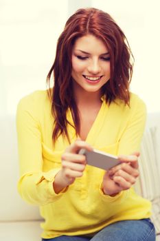 home, technology and internet concept - smiling woman playing with smartphone sitting on couch at home